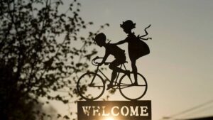 sculpture en fer forgé composé de deux silhouettes d'enfants sur un vélo avec le message Welcome